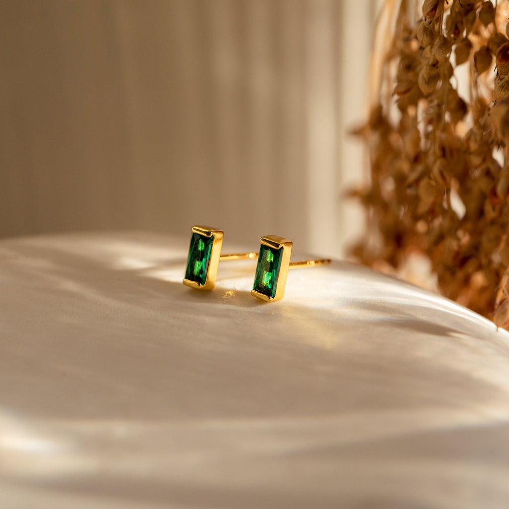 Baguette Birthstone Studs featuring rectangular green stones are shown on a white surface in soft, natural light—ideal as personalized gifts for any occasion.