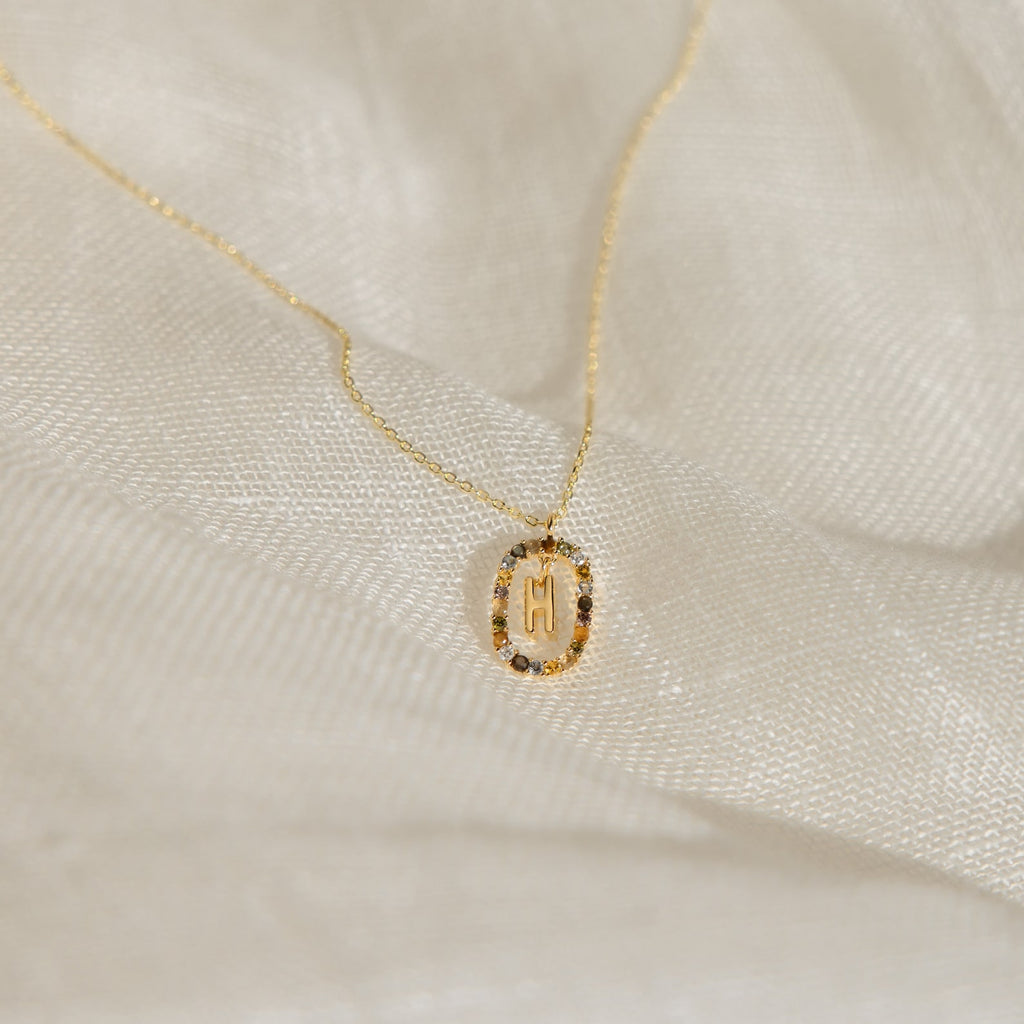 Rainbow Initial Necklace featuring a round pendant engraved with the letter M, displayed on soft white fabric—a timeless personalized piece perfect for adding a special touch to any style.