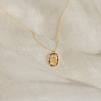 Rainbow Initial Necklace featuring a round pendant engraved with the letter M, displayed on soft white fabric—a timeless personalized piece perfect for adding a special touch to any style.