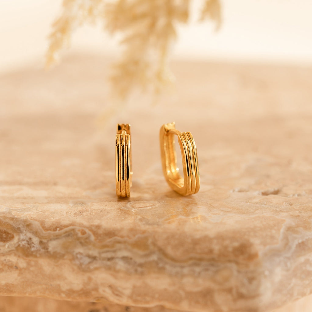 Two Ribbed Link Hoops with a ribbed rectangle design rest on a beige marble surface, their geometric style complemented by the soft, neutral background.