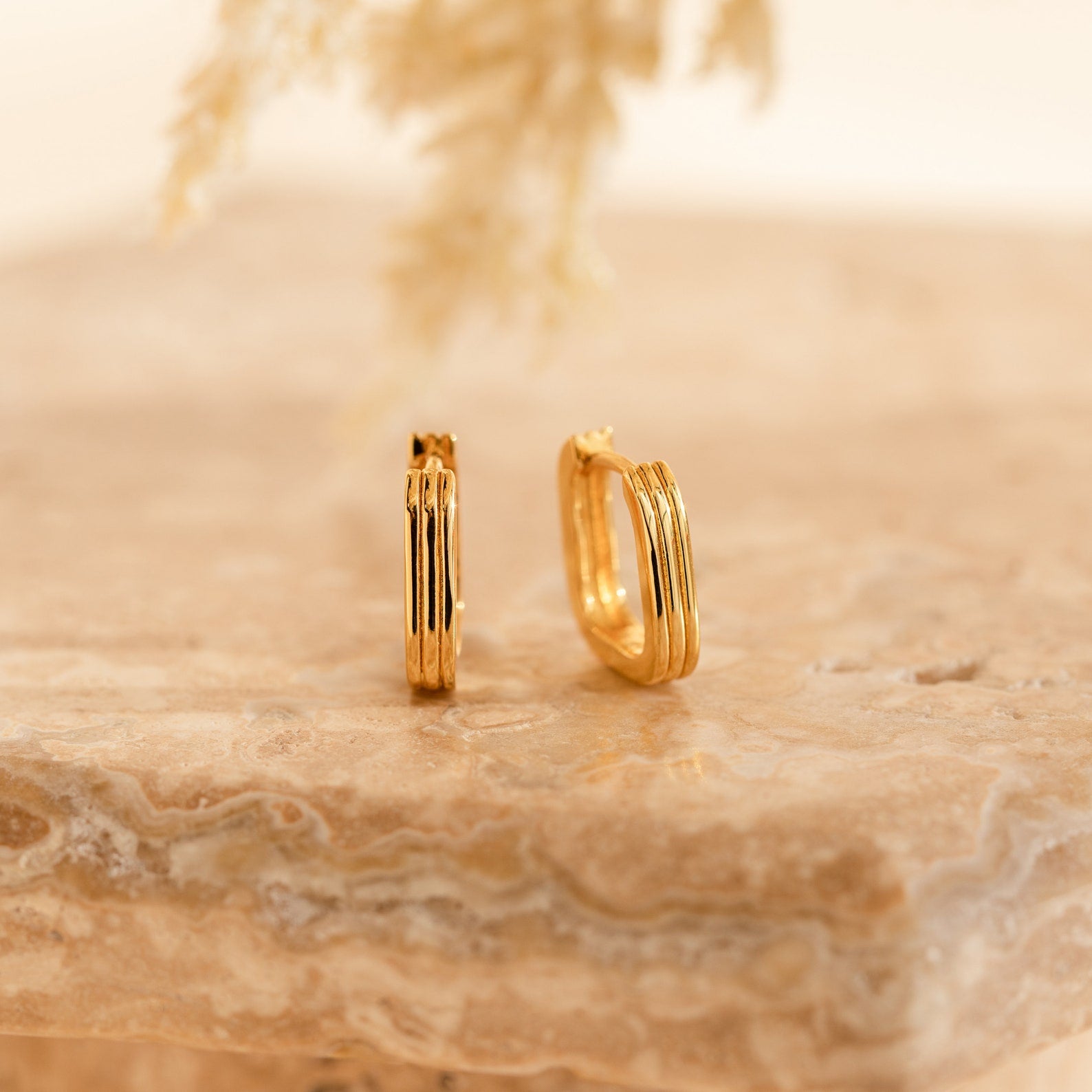 Two Ribbed Link Hoops with a ribbed rectangle design rest on a beige marble surface, their geometric style complemented by the soft, neutral background.