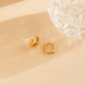 Two Ribbed Link Hoops rest beside a faceted clear glass object on a beige surface, adding a modern geometric earrings touch.