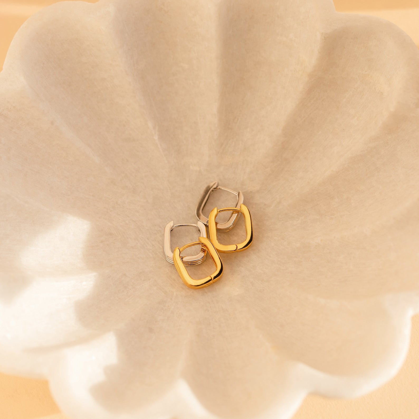 Ribbed Link Hoops in two-tone gold and silver are displayed on a white, petal-shaped dish, highlighting their chic geometric square hoop design.