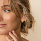 A woman with wavy blonde hair touches her face, showing off her manicured nails and chic Ribbed Link Hoops.