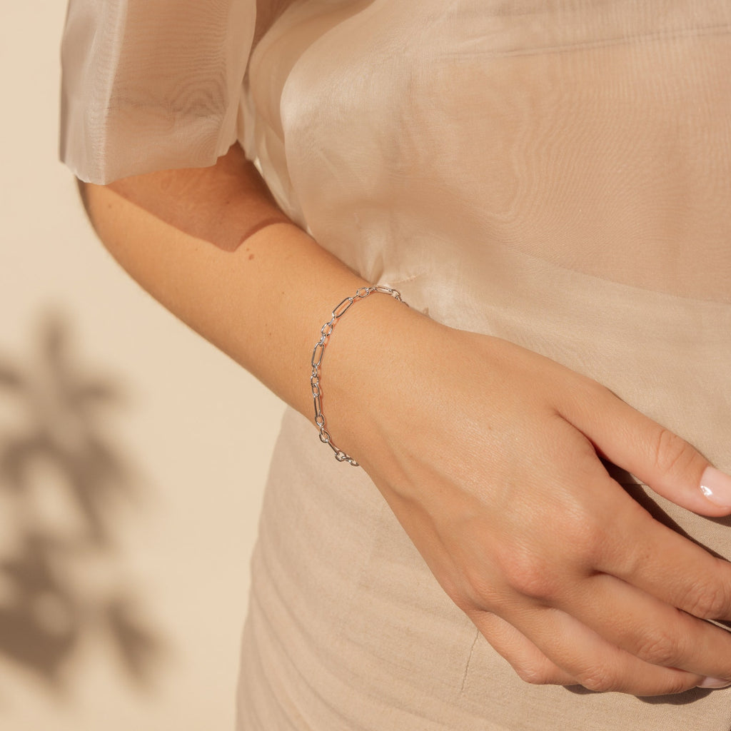 A hand adorned with the Roxy Paperclip Chain Bracelet rests against a beige sheer dress, showcasing a touch of minimal jewelry elegance.