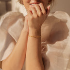 A woman smiles, wearing a sheer ruffled white top and the Roxy Paperclip Chain Bracelet on her wrist for a touch of minimal jewelry.