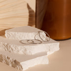 The Skinny Stacking Rings Set is displayed on white stone slabs, with a wooden object and brown vase in the background—perfect for those who love minimalist rings.