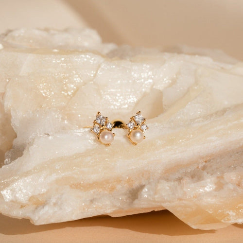 Angelina Pearl Studs, featuring elegant pearls and sparkling crystals, are displayed on a textured, light-colored stone background.