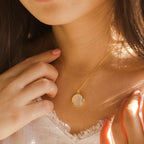 Close-up of a woman gently touching her Endless Love Locket Necklace, featuring a gold chain and round, clear pendant.