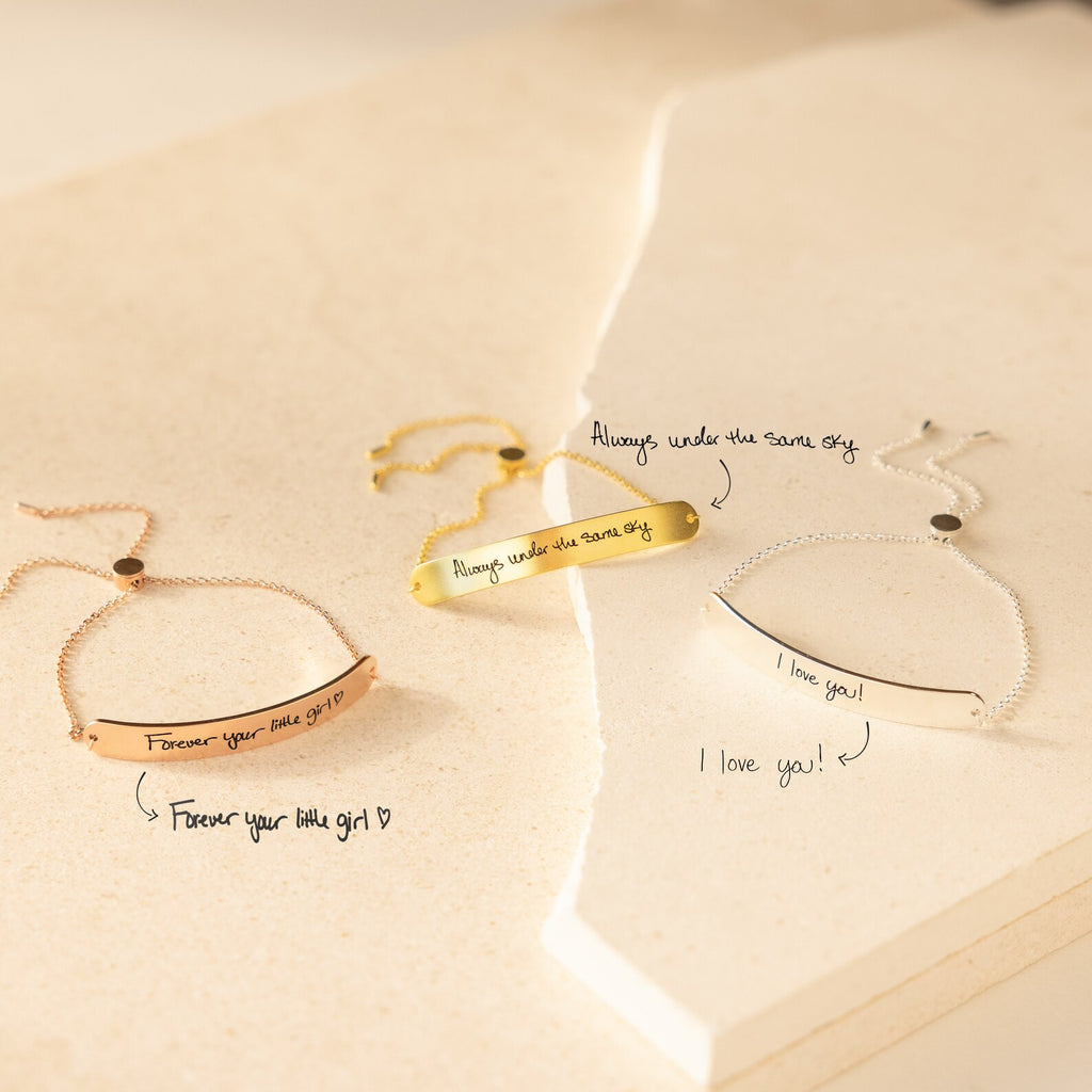 Three engraved Slider Handwriting Bracelets rest on a cream surface, each personalized with a heartfelt handwritten message—perfect as a meaningful gift.