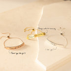 Three engraved Slider Handwriting Bracelets rest on a cream surface, each personalized with a heartfelt handwritten message—perfect as a meaningful gift.