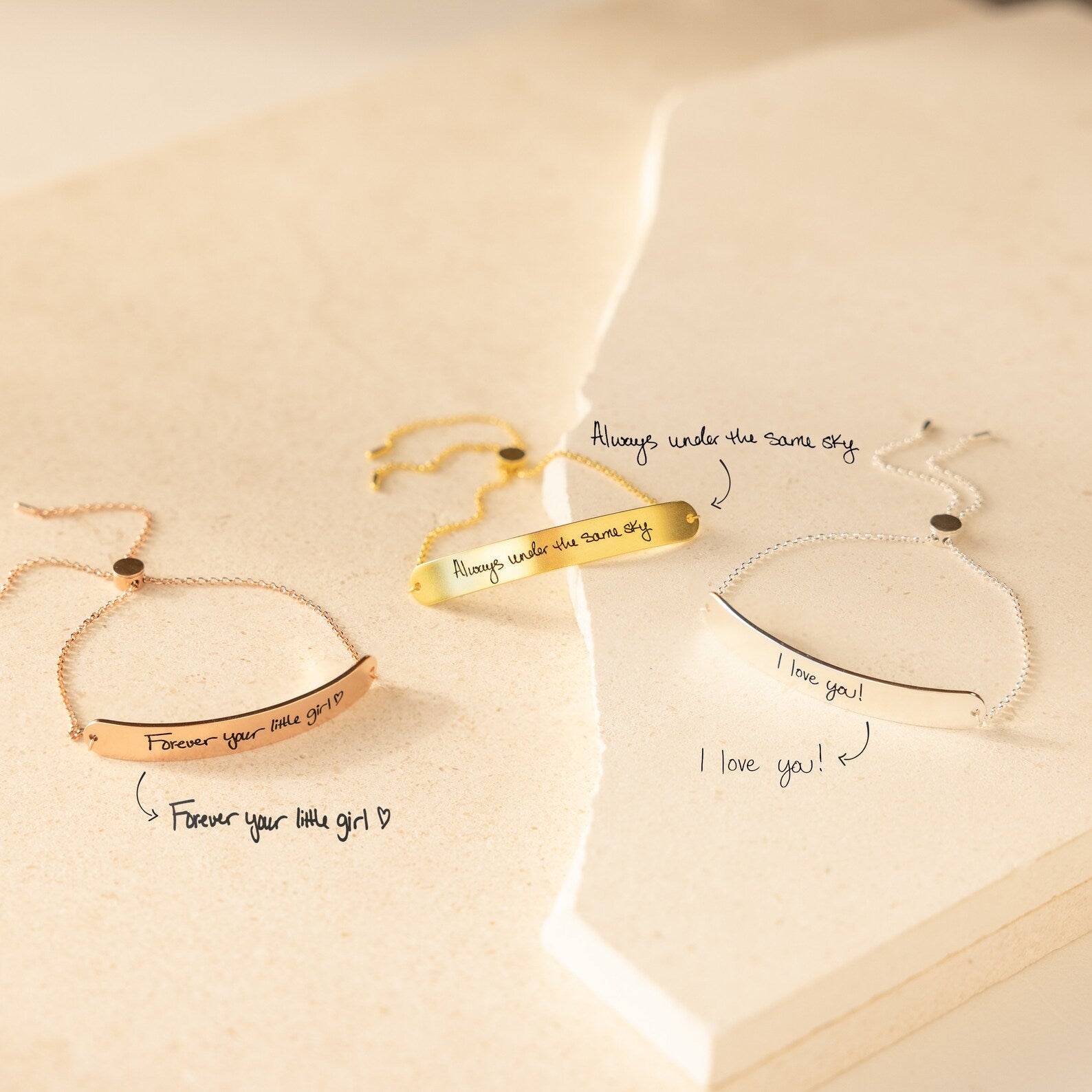 Three engraved Slider Handwriting Bracelets rest on a cream surface, each personalized with a heartfelt handwritten message—perfect as a meaningful gift.