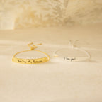 Two Slider Handwriting Bracelets—one gold engraved with "You’re My Person" and one silver with "I love you!"—rest on a beige surface, making ideal personalized keepsakes to cherish daily.