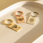 Three Fingerprint Rectangle Keychains with engraved fingerprints forming hearts rest on a white tray in sunlight—a perfect personalized keepsake.