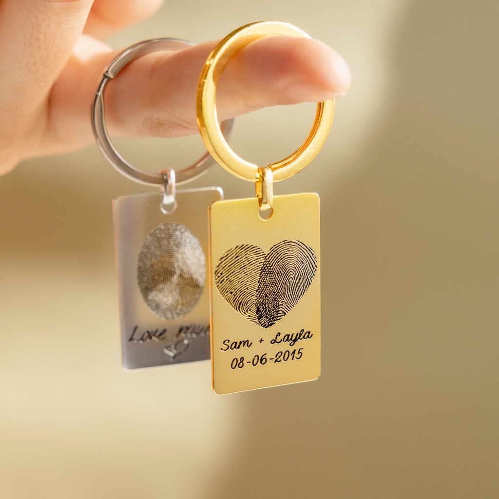 Two Fingerprint Rectangle Keychains—one gold with "Sam + Layla 08-06-2015" and one silver—create a meaningful personalized keepsake.