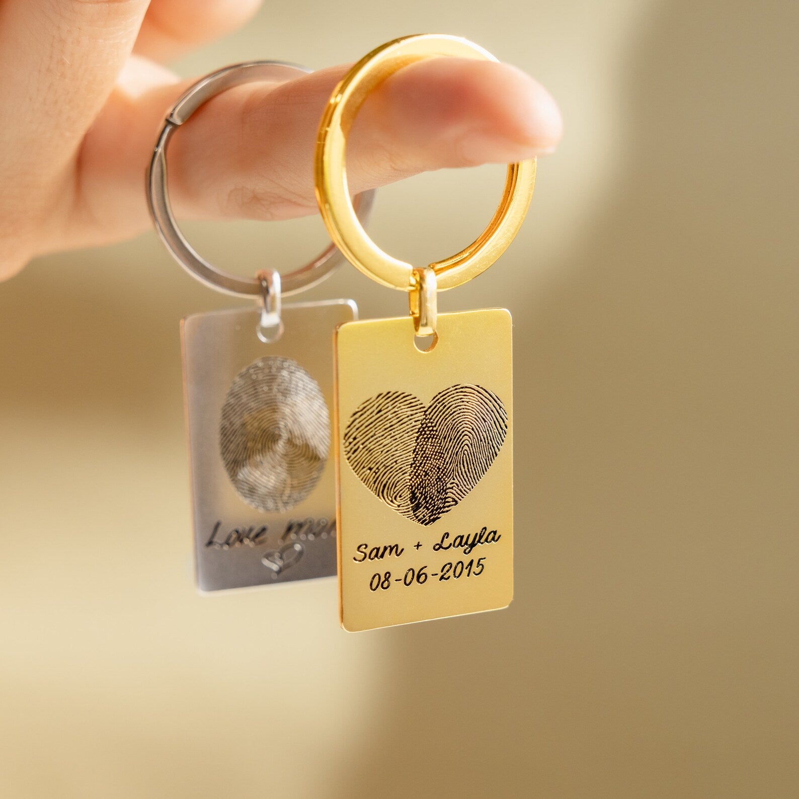 Two Fingerprint Rectangle Keychains—one gold with "Sam + Layla 08-06-2015" and one silver—create a meaningful personalized keepsake.