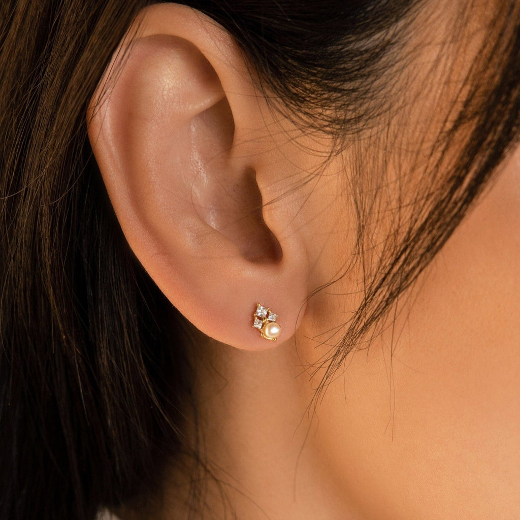 Close-up of a woman's ear wearing Angelina Pearl Studs—elegant pearl earrings adorned with tiny sparkling stones for a sophisticated touch.
