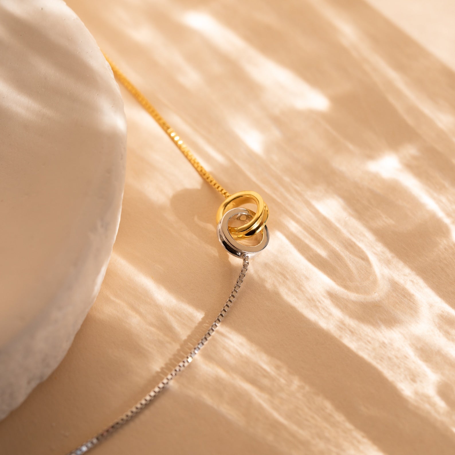 Interlocking Circles Bracelet on a beige surface with soft, wavy light reflections—a perfect anniversary gift for those who appreciate refined elegance.