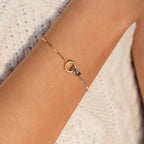 The Interlocking Circles Bracelet, featuring minimalist gold and silver rings, is shown on a wrist against cream knit fabric—an elegant charm bracelet ideal as an anniversary gift.