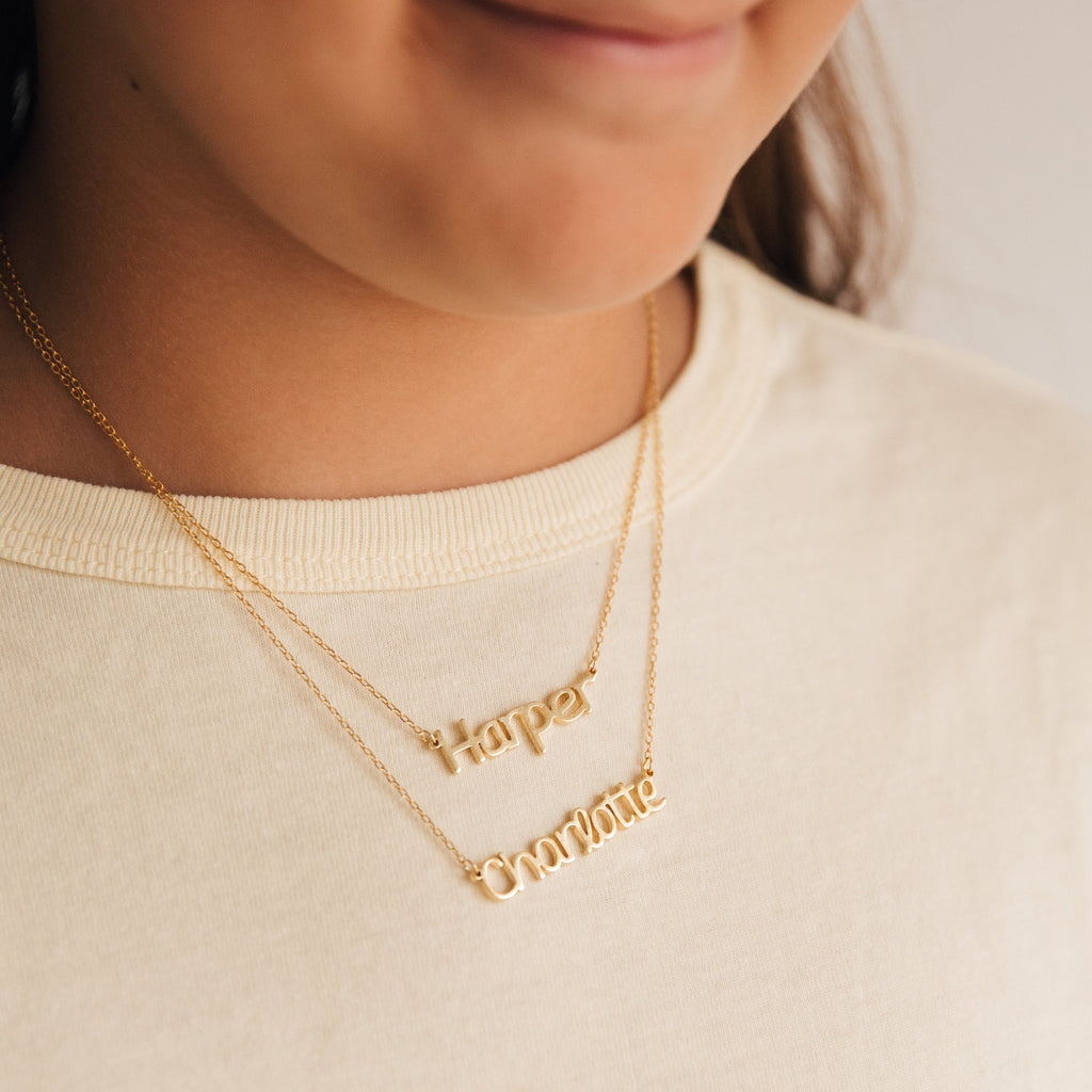 Close-up of a child wearing two Maine Kid's Name Necklaces, each personalized with "Harper" and "Charlotte," highlighting stylish, customized kids jewelry.