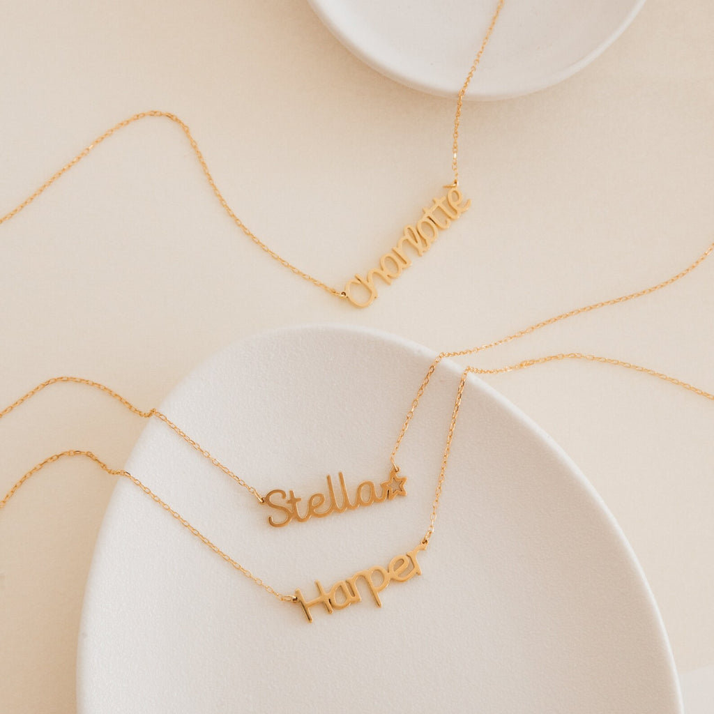 Three gold Maine Kid’s Name Necklaces reading Charlotte, Stella, and Harper are displayed on white trays—perfect as a personalized piece or a thoughtful addition to any kids jewelry collection.
