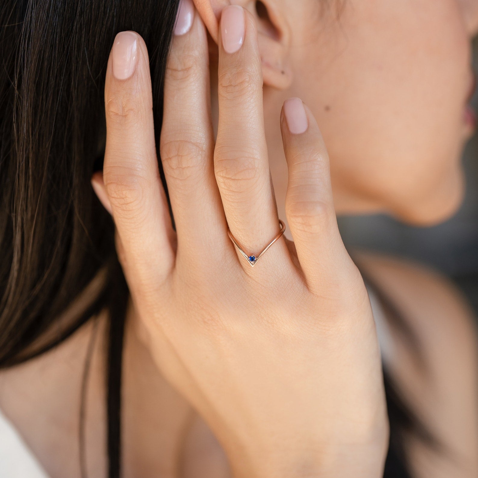 Close-up of a woman’s hand with nude nails, wearing a delicate gold Chevron Birthstone Ring featuring a small blue gemstone.