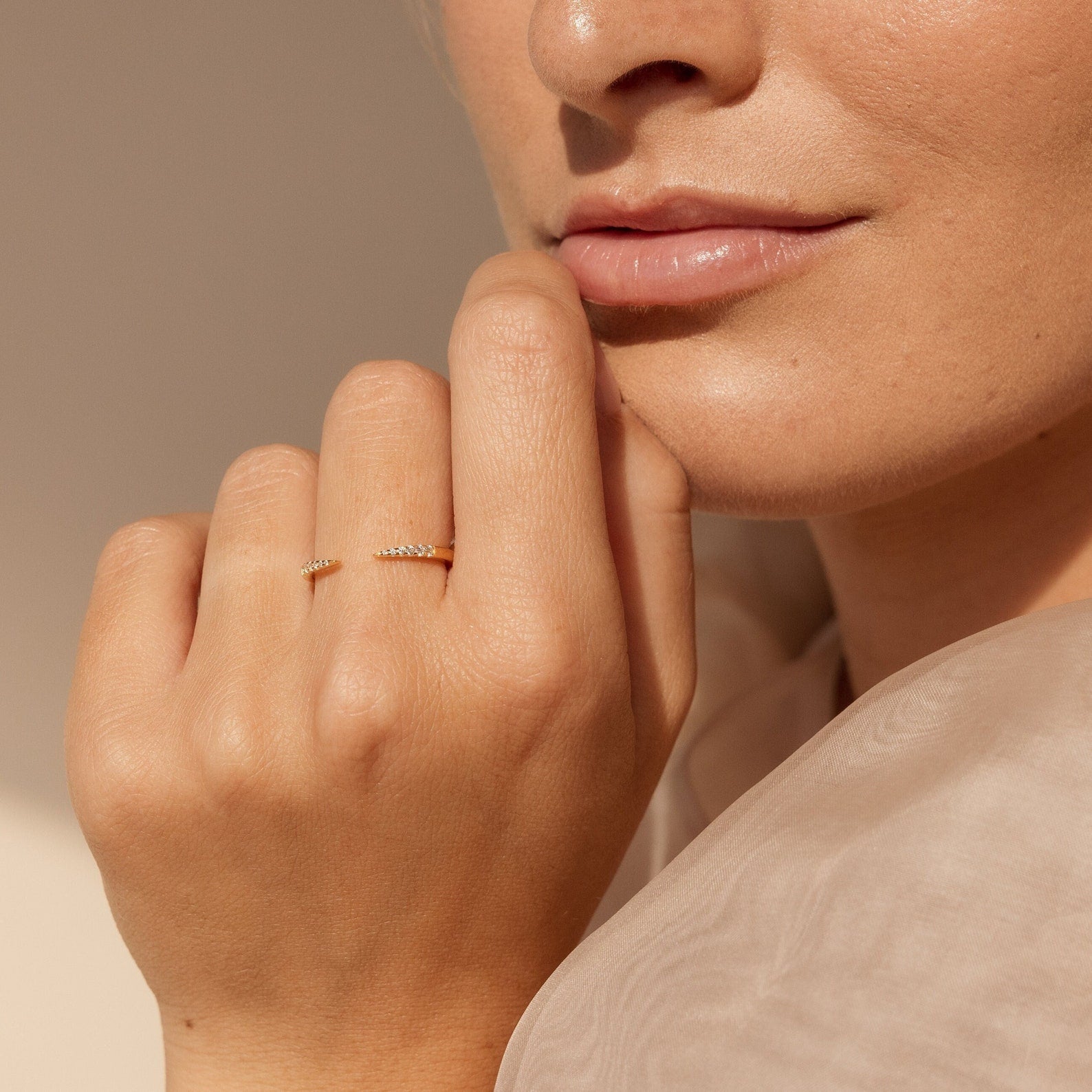 A woman's hand with the Jessie Duo Pave Ring, a dainty gold pavé open ring, rests near her face, accentuated by natural makeup and soft lighting.