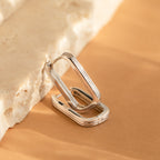 Large Ribbed Link Hoops in silver, featuring a rectangular ribbed design, rest against a textured beige stone on a tan surface, exemplifying minimalist jewelry style.