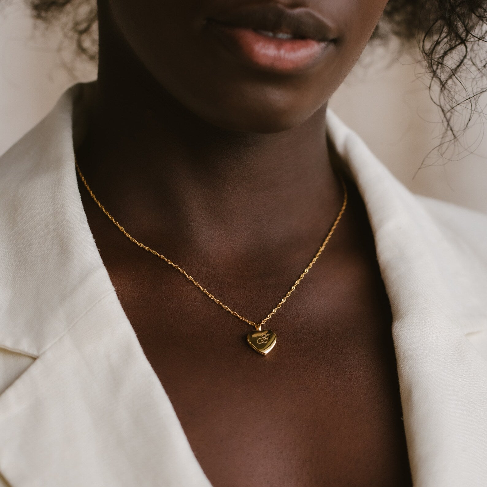 A woman wearing the Initial Heart Locket Necklace and a cream-colored blazer.