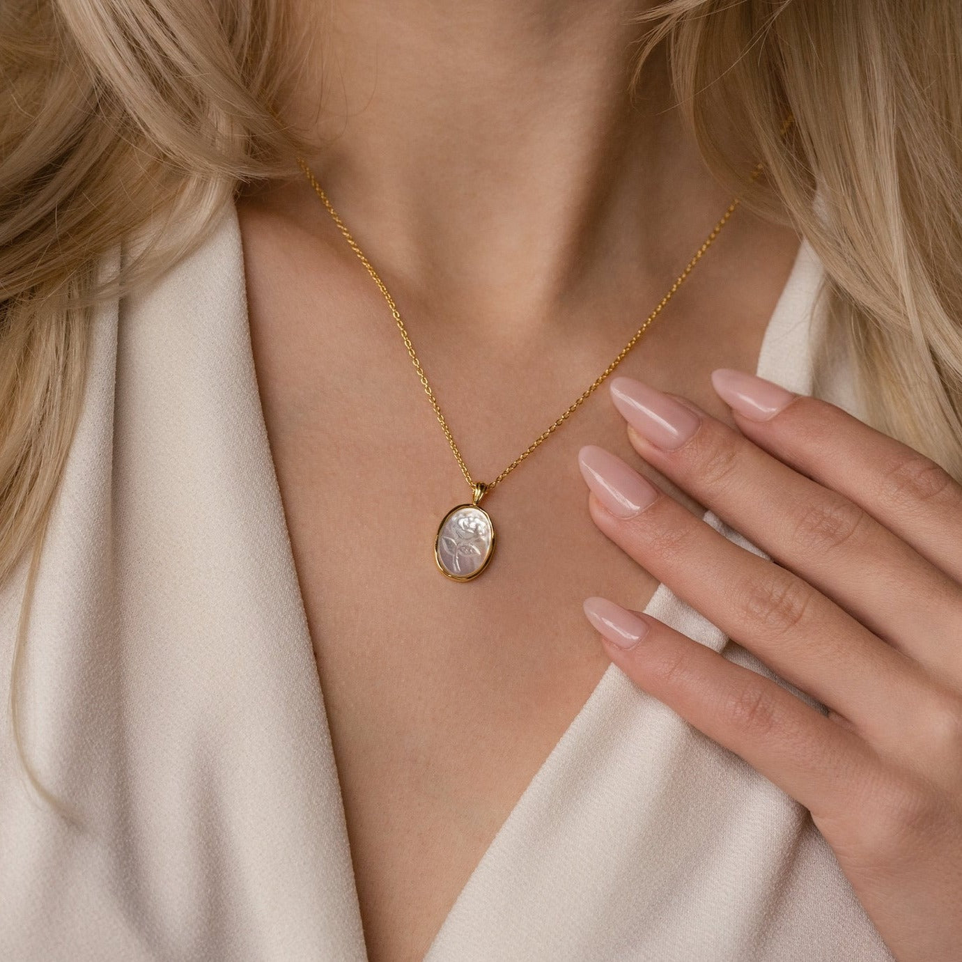 A woman wears a Vintage Rose Necklace with an oval pendant, her manicured nails gently touching her chest.