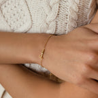 The Venice Tiny Name Bracelet, a minimal jewelry piece with a cursive gold name, adds an elegant touch when paired over a cream knit sweater.