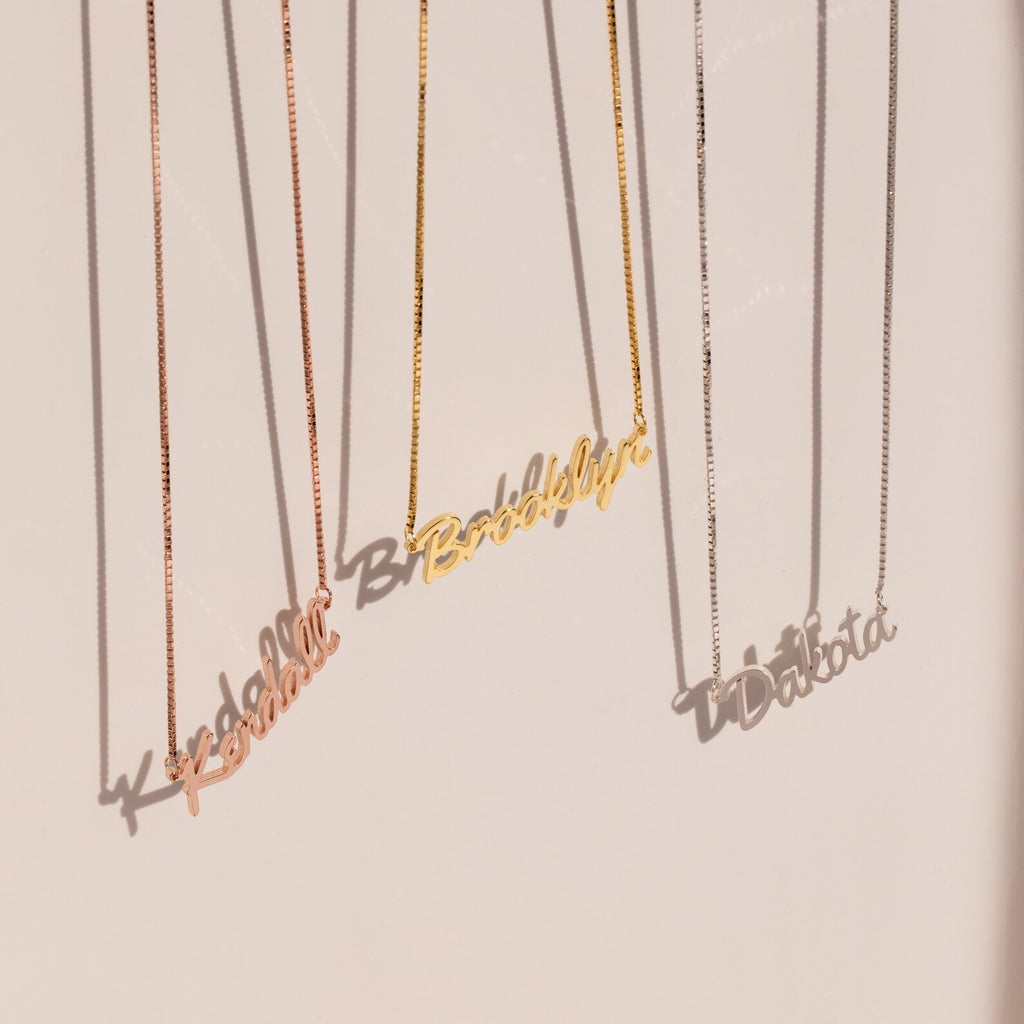 Three Casella Name Necklaces in box chains, each personalized with Kendall, Brooklyn, and Dakota in a dainty script font, hang elegantly—perfect as a custom gift.
