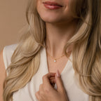 Woman with long blonde hair wears a cream top and holds the Tabitha Opal Drop Necklace, featuring a small teardrop charm—an ideal romantic gift.