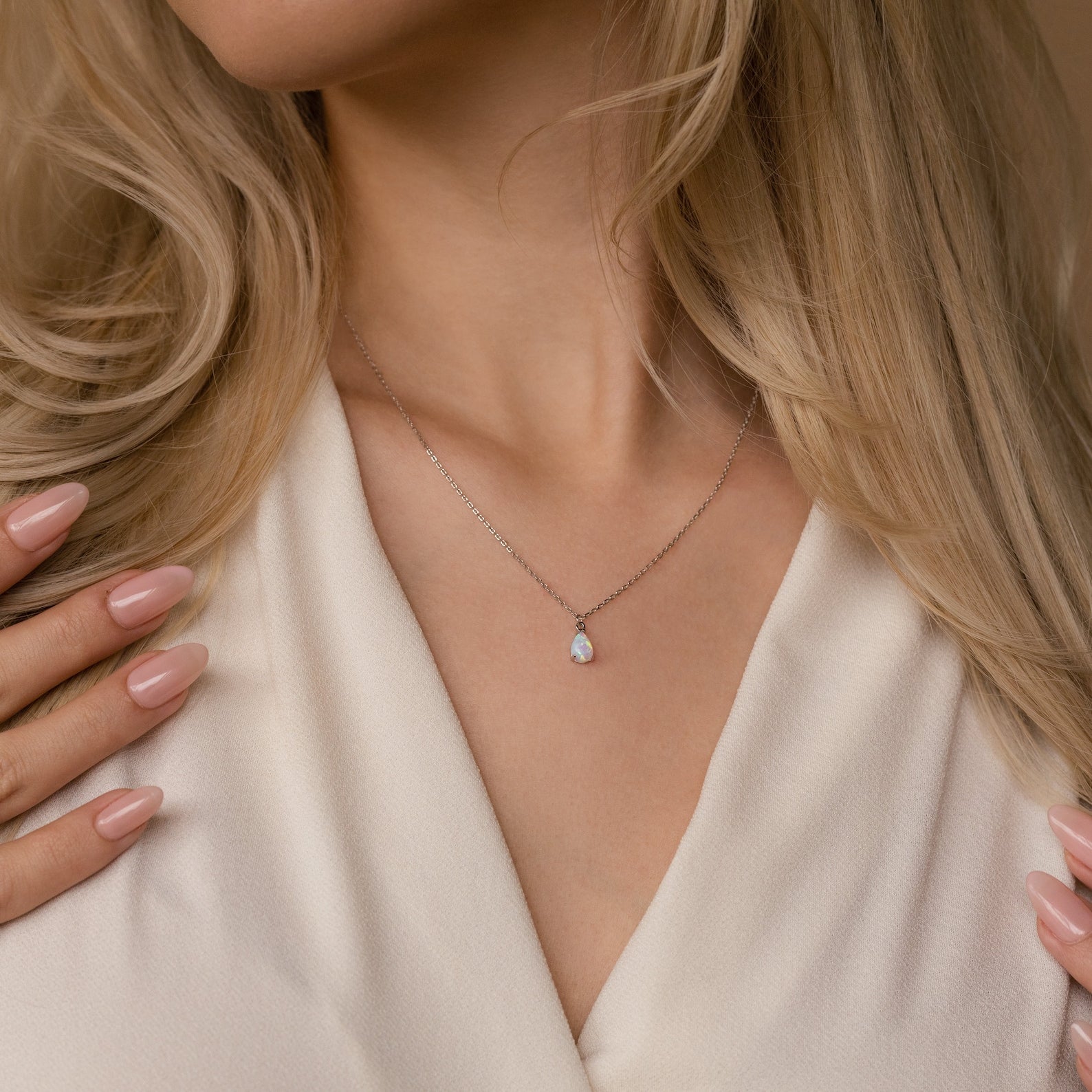 A woman wears the Tabitha Opal Drop Necklace featuring a delicate teardrop opal charm with her cream V-neck blouse—a perfect romantic gift.
