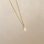 A gold chain necklace featuring a small, iridescent teardrop charm pendant—the Tabitha Opal Drop Necklace—displayed on a light beige background, perfect as a romantic gift.