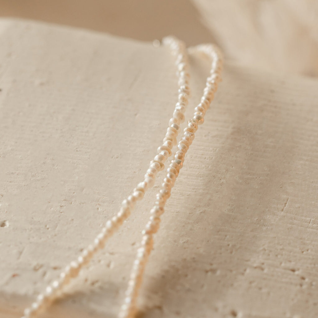 Flat-lay image of the pearl choker arranged on textured beige surface, highlighting off white color and irregular shaped pearls. 