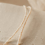 Flat-lay image of the pearl choker arranged on textured beige surface, highlighting off white color and irregular shaped pearls. 