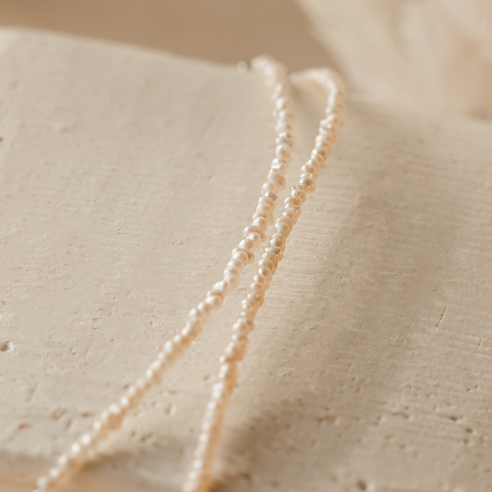 Flat-lay image of the pearl choker arranged on textured beige surface, highlighting off white color and irregular shaped pearls. 