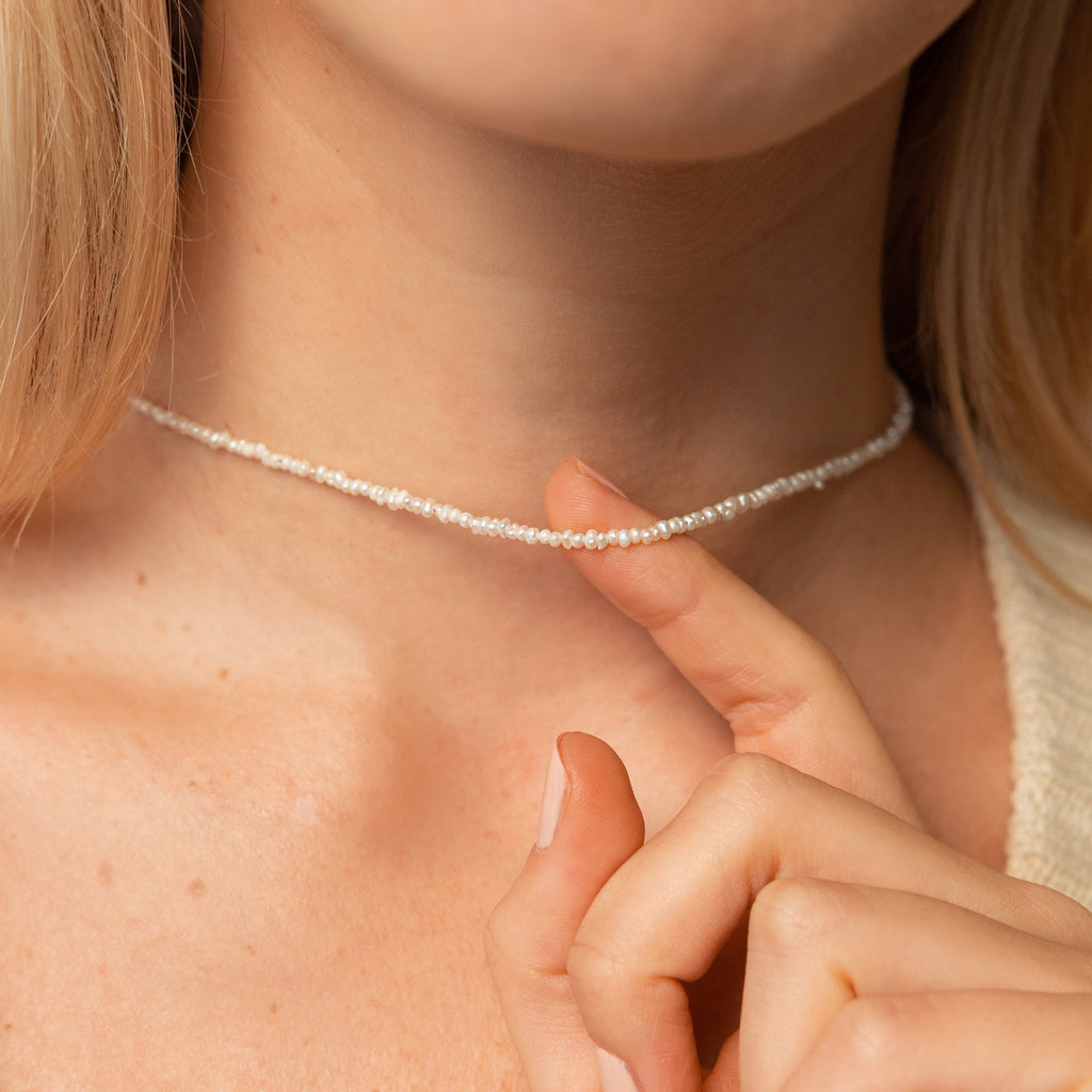 Close-up of a woman’s neck and upper chest wearing the Pearl Choker in 18K gold, with her hand gently resting near the necklace—showing delicate pearls and fine chain.