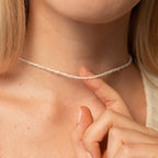 Close-up of a woman’s neck and upper chest wearing the Pearl Choker in 18K gold, with her hand gently resting near the necklace—showing delicate pearls and fine chain.