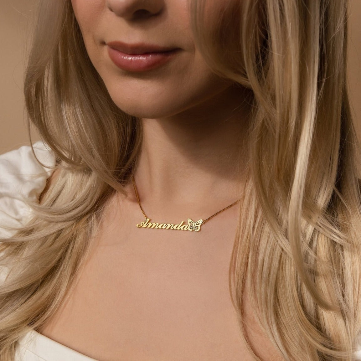 A woman shown from the shoulders up wears the Butterfly Name Necklace in Box Chain, personalized with “Amanda” and featuring a delicate gold butterfly charm.
