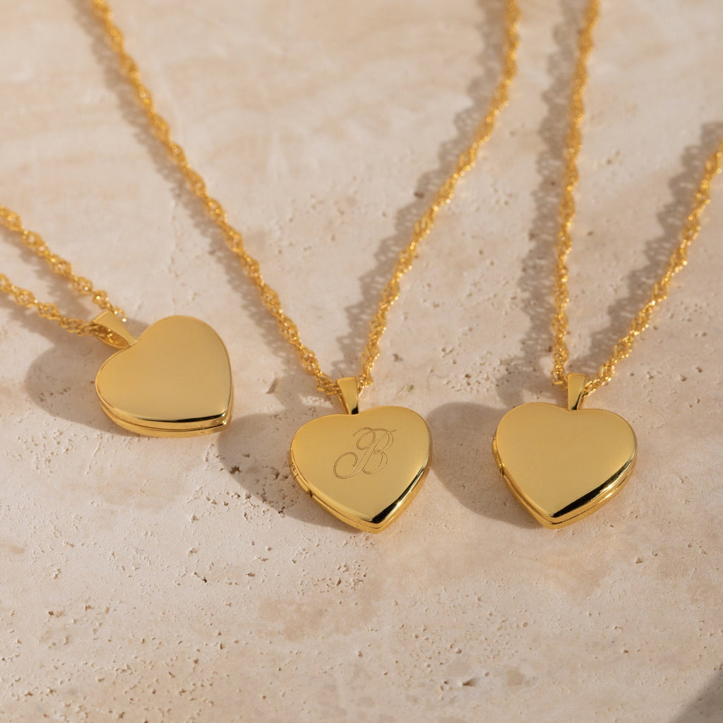 Three Initial Heart Locket Necklaces on gold chains, ideal for personalized jewelry, elegantly displayed on a light beige surface.