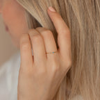 A hand adorned with the Thin Mini Birthstone Ring, its petite blue stone shining, brushes through long blonde hair—making it an ideal minimalist accessory and a thoughtful Christmas gift.