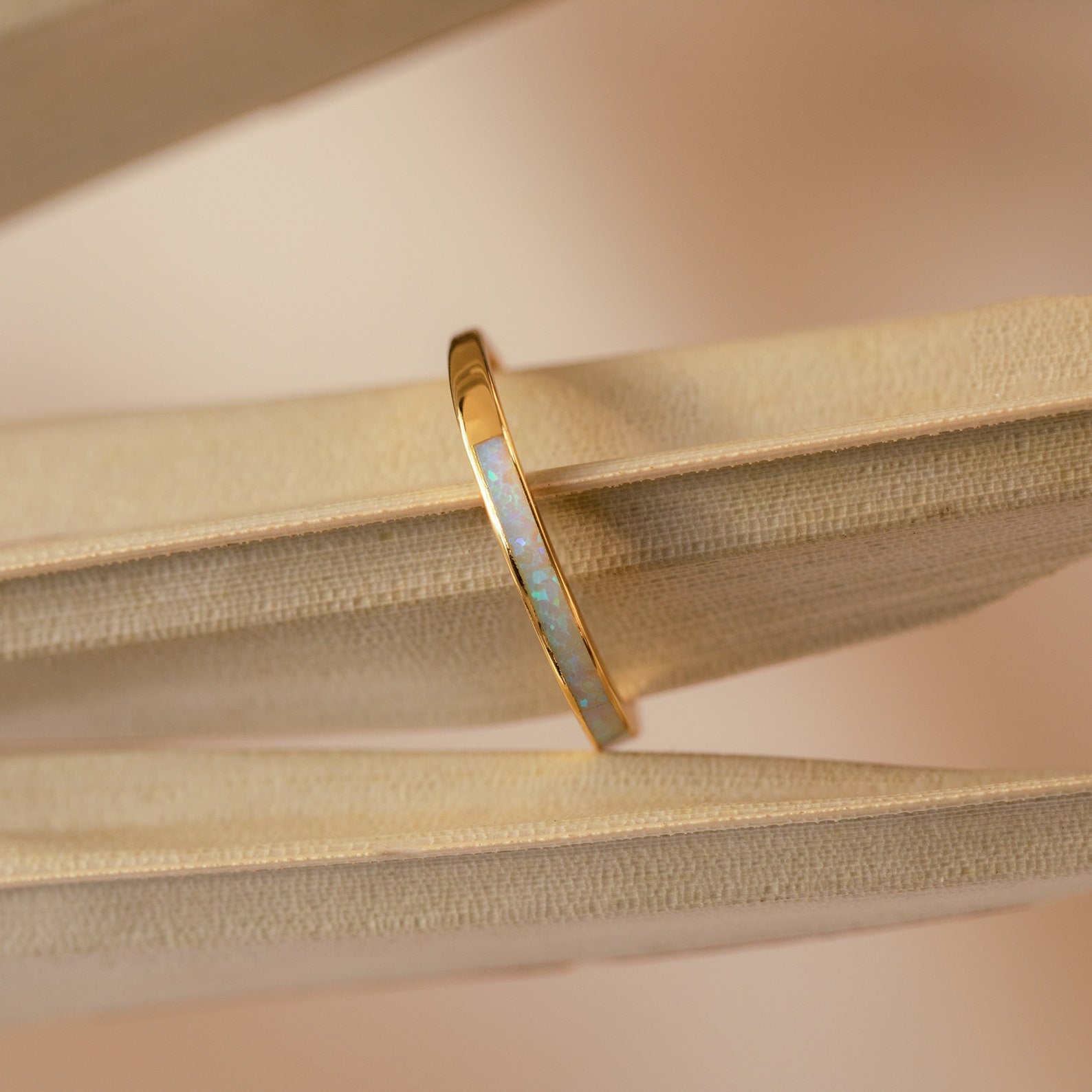 The White Opal Inlay Band in 18K Gold rests on the pages of an open book, showcasing its striking gemstone design.
