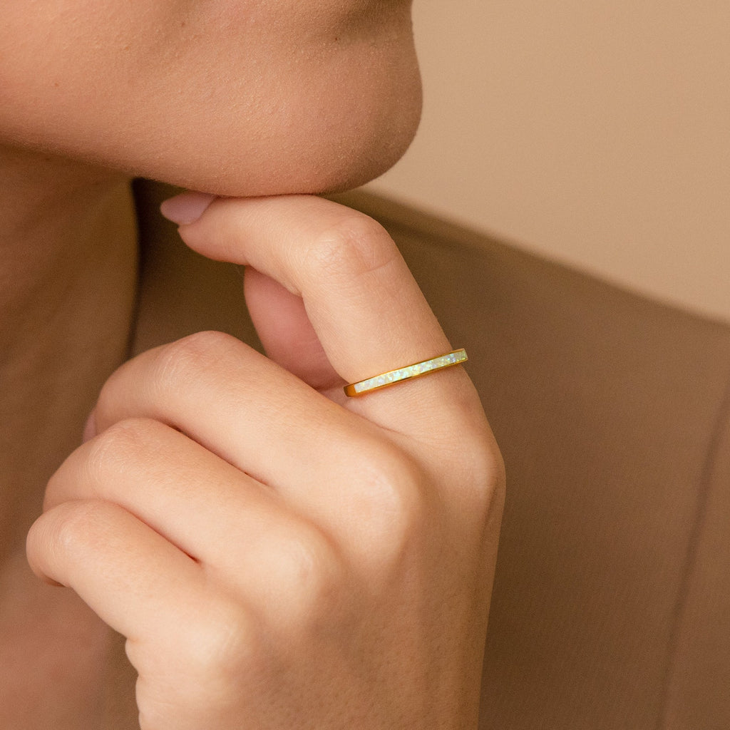 A hand wearing a White Opal Inlay Band touches a chin; the person is dressed in a brown jacket.