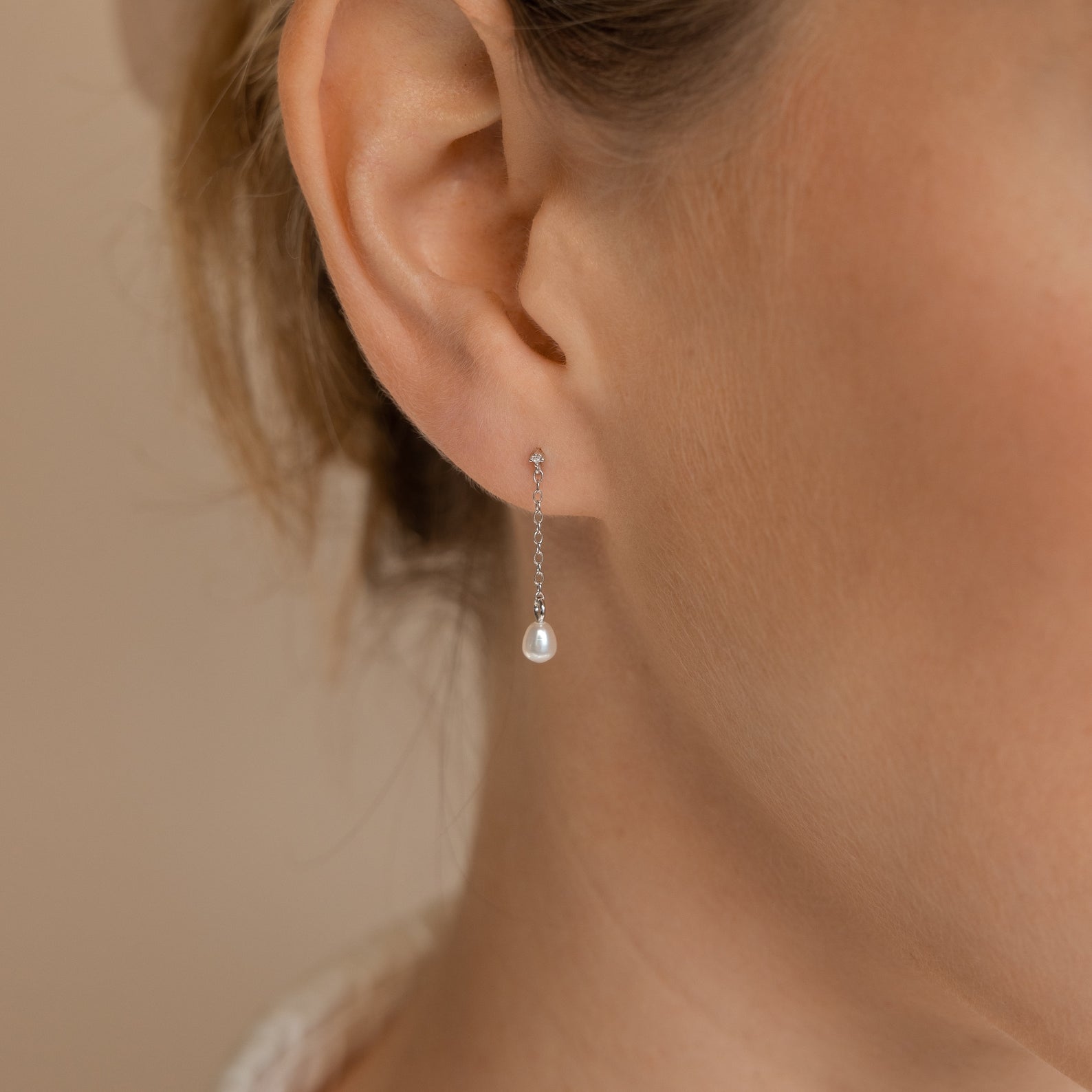 Close-up of a woman's ear adorned with the Isha Pearl Drop Earrings in Sterling Silver, featuring a delicate silver chain and a dangling pearl—ideal for lovers of subtle elegance.