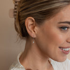 A light-haired woman with a claw clip smiles against a neutral background while wearing the Isha Pearl Drop Earrings.