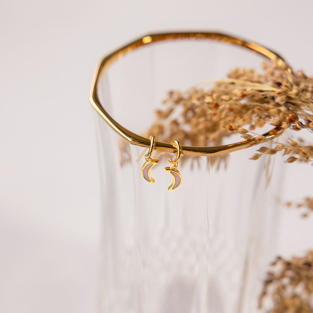 Opal Moon Mini Hoops: gold huggie earrings with two crescent moons, perfect for stacking. Shown displayed on a ribbed glass vase with dried flowers.