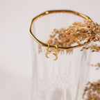 Opal Moon Mini Hoops: gold huggie earrings with two crescent moons, perfect for stacking. Shown displayed on a ribbed glass vase with dried flowers.