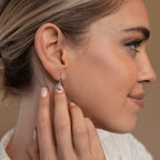 A woman touches a small silver Opal Moon Mini Hoop Earring with an opal moon charm, her hair tied back and perfectly styled for an elegant earring stack.